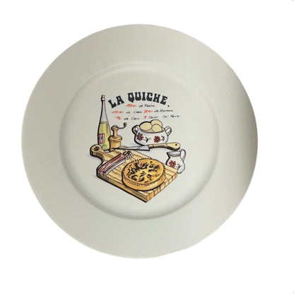 White plate with 'La Quiche' illustration featuring a pie, eggs, and other kitchen items on a white background.