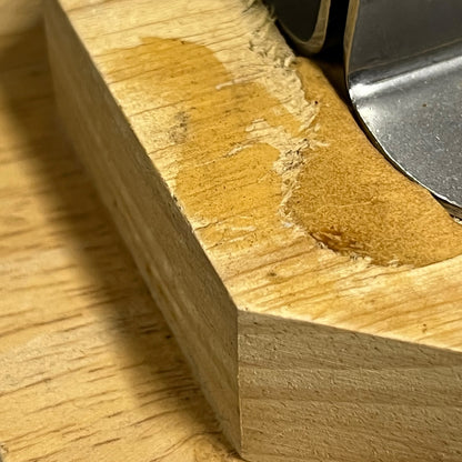 Close-up of a light natural wood block with a worn, polished area showing the wood grain and a metal object partially visible at the top right.