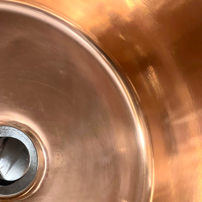 Close up of French copper bowl upcycled into a copper sink with iron handles and a chrome pop up waste on a white background