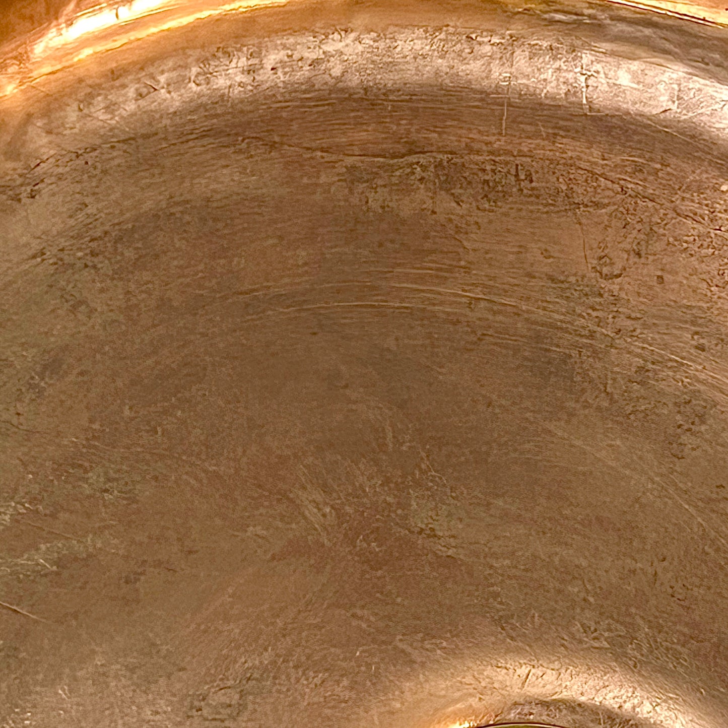 Close-up of a metallic bronze or copper surface with a brushed, textured finish and warm reflective highlights.