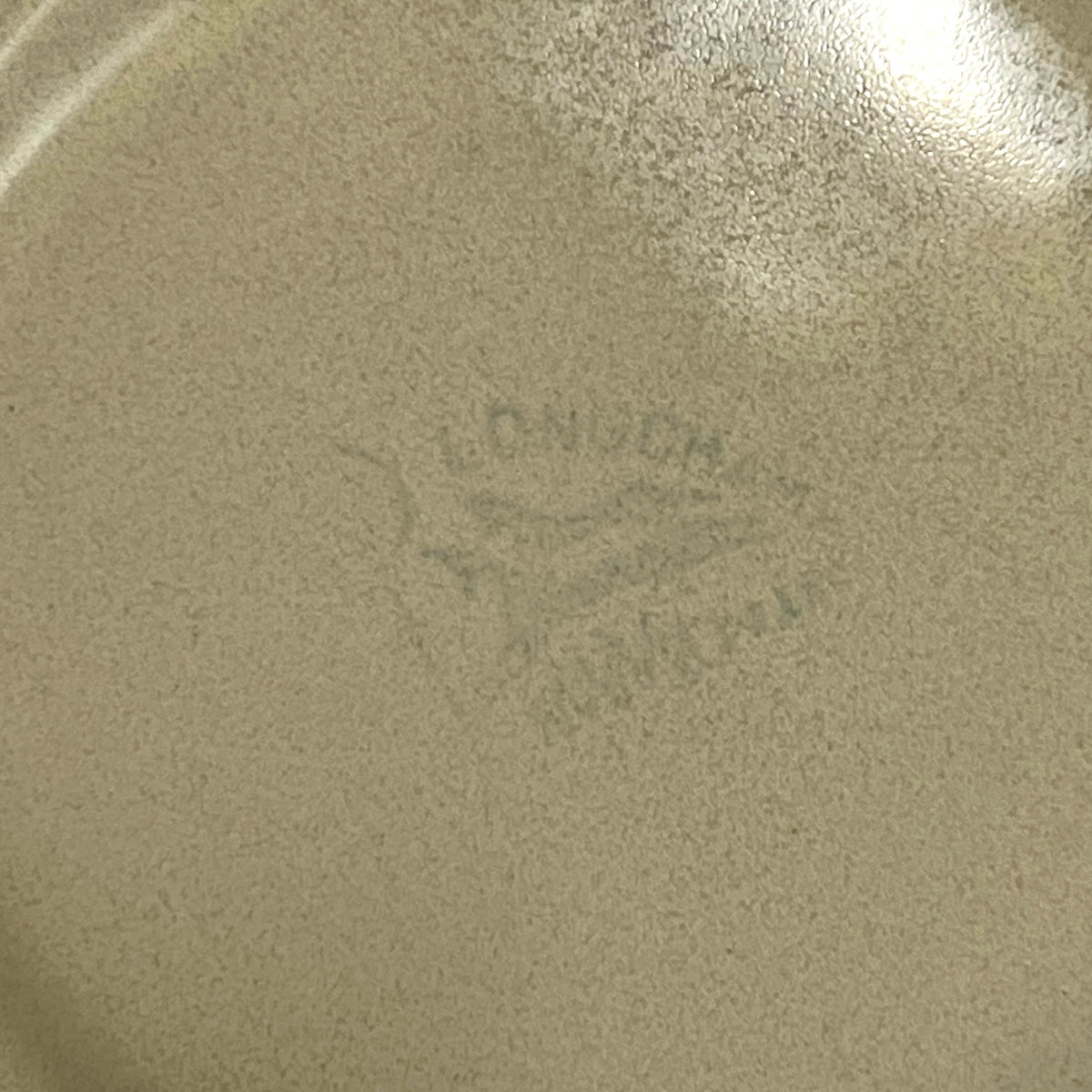 Close-up of the bottom of a speckled beige ceramic pan or plate with a faint  Longchamp mark in the centre.