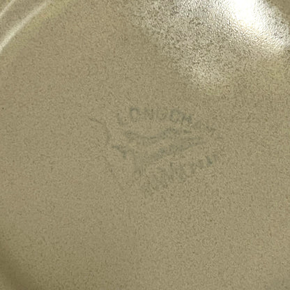 Close-up of the bottom of a speckled beige ceramic pan or plate with a faint  Longchamp mark in the centre.