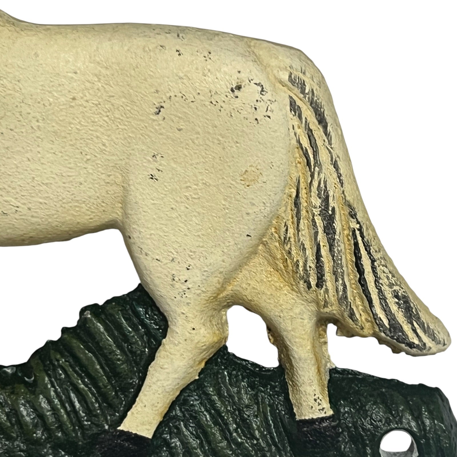 A close-up of a horse figurine or decorative sculpture showing the side and rear of a light beige horse standing on a dark textured base, photographed against a plain white background.