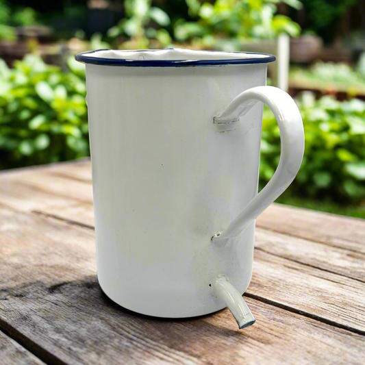 White enamel mug with blue rim and spout on a wooden surface outdoors