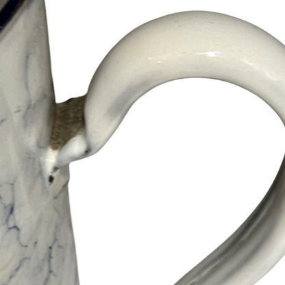 Close-up of a blue and  white pot handle and part of the marbled white body with subtle blue veining, isolated on a white background.