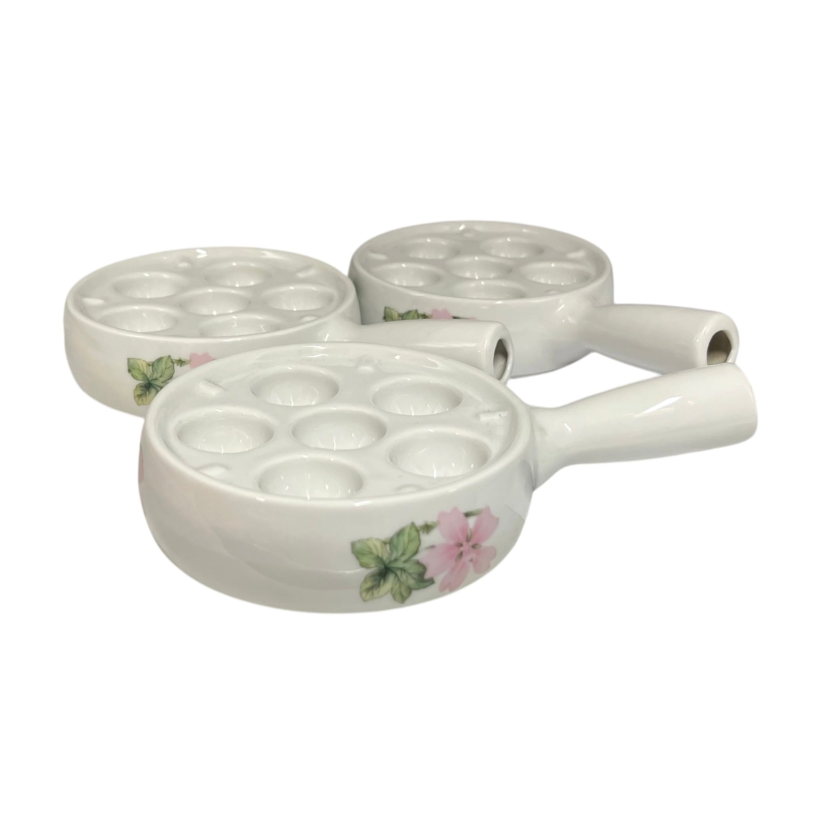 Three white ceramic egg or snail plates with floral pink and green accents, arranged on a plain white background.