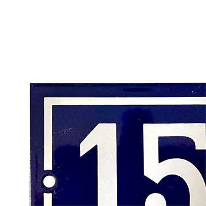 Close-up of a dark blue square sign with white border lines and large white numerals '15' on a white background.