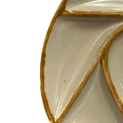 Close-up of a ceramic plate with a leaf-like segmented design, featuring a glossy beige glaze and thick brown painted outlines, set against a plain white background.