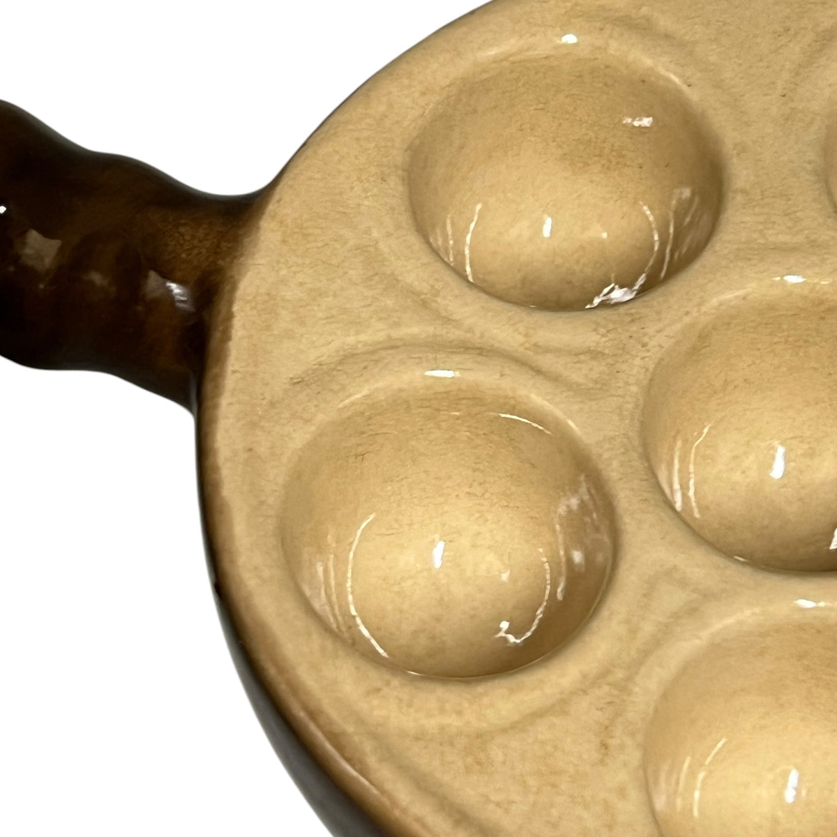 Close-up of a ceramic snail plates with 6 deep oval indentations and a dark brown handle, shown on a white background.