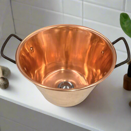 Copper upcycled basin sink or washbowl with a chrome waste and black handles on a white background with houseplants 