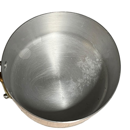 An empty aluminium lined copper saucepan viewed from directly above, showing a brushed metal interior with some light scuffs and a small brass handle attachment visible on the left