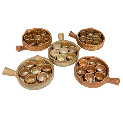 Five rustic brown ceramic serving dishes with small cup holders, arranged on a plain white background.