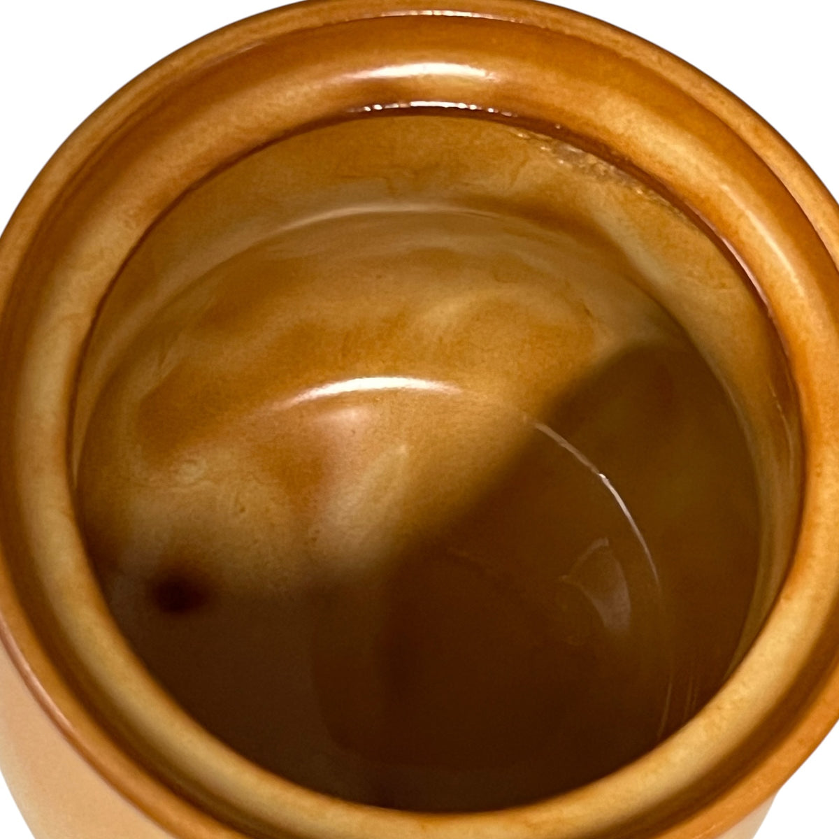 A close-up top-down view of a glossy brown ceramic pot or container with a warm amber-brown glazed finish, set against a plain white background.