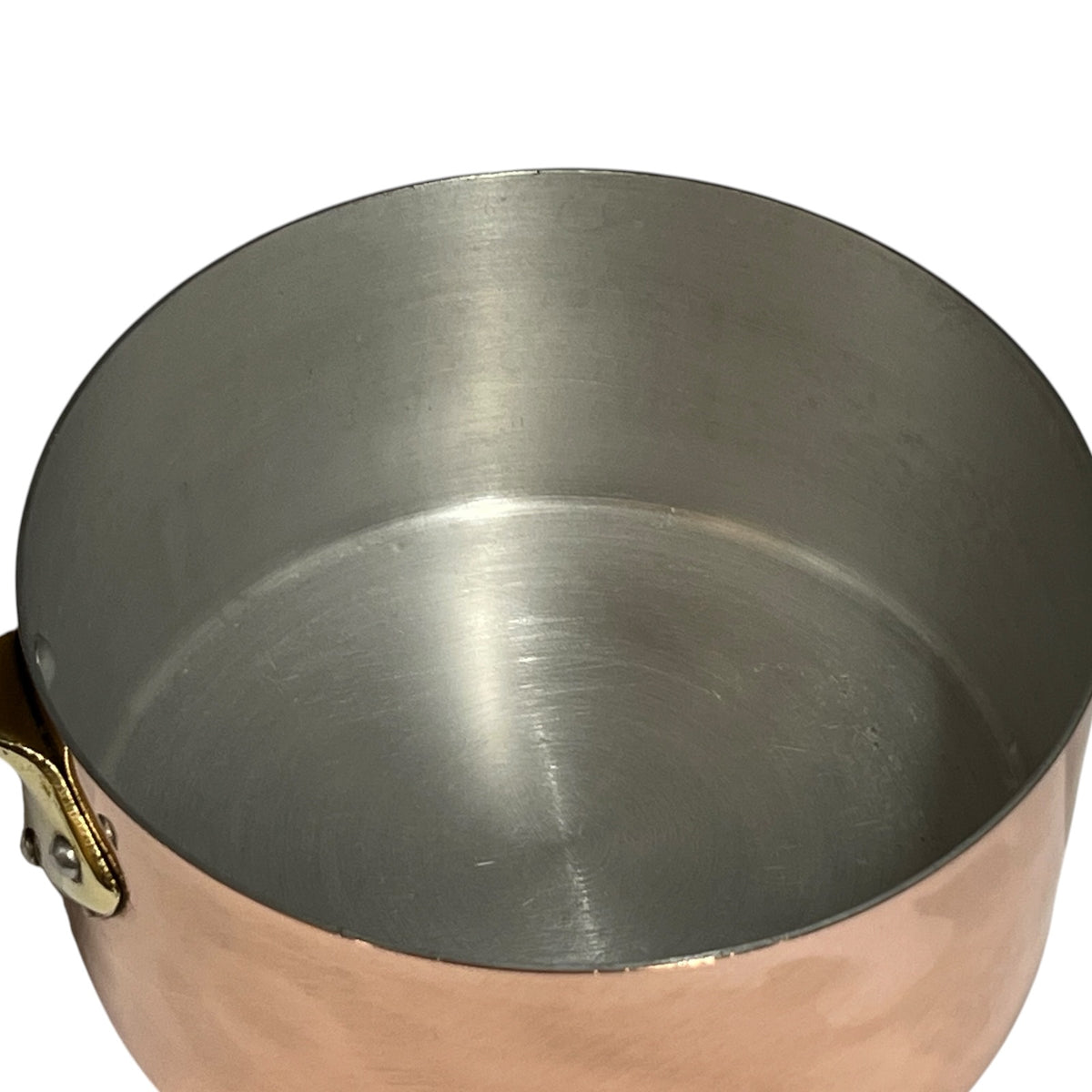 A close-up of a copper saucepan or pot with a brushed stainless steel interior and a brass handle clasp, shown against a plain white background.