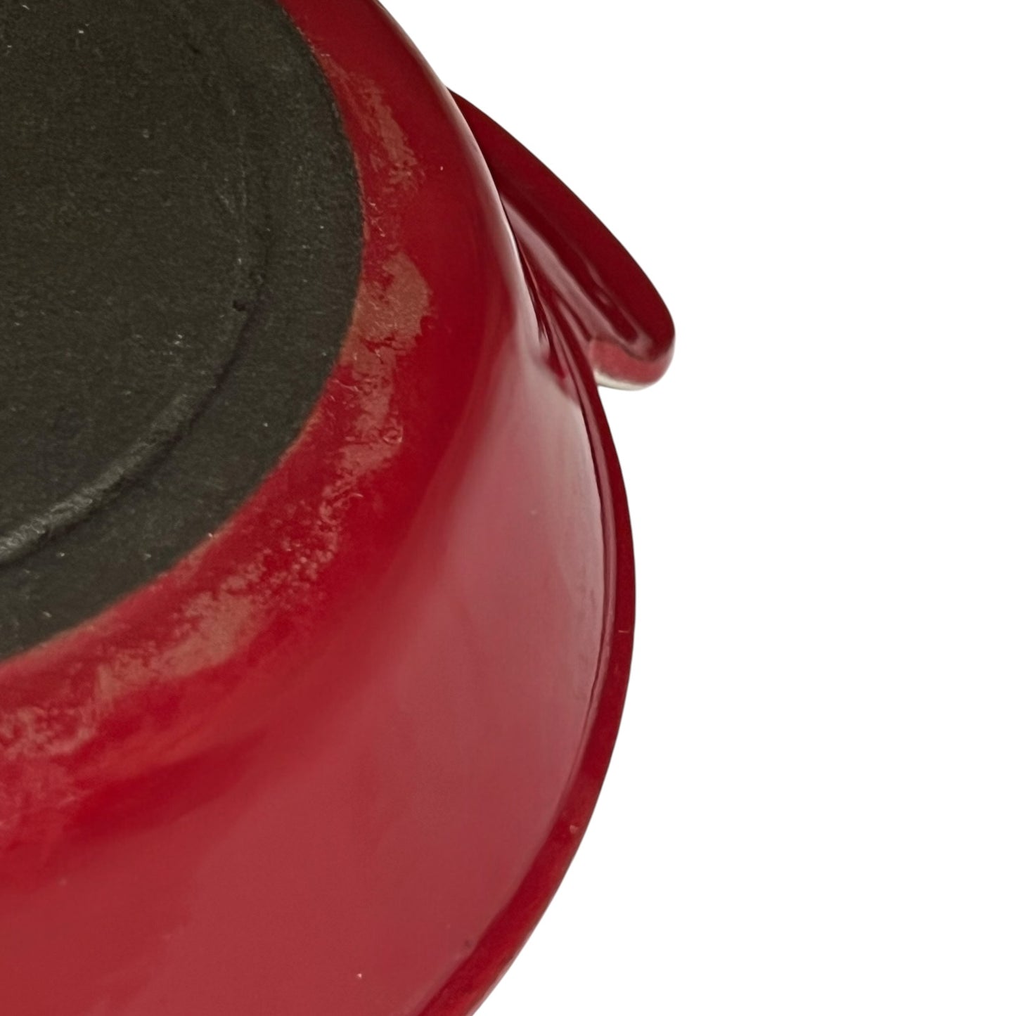 Close-up detail of a red enameled cast iron pot or pan showing the glossy red exterior and a dark non-stick coated interior, on a white background.