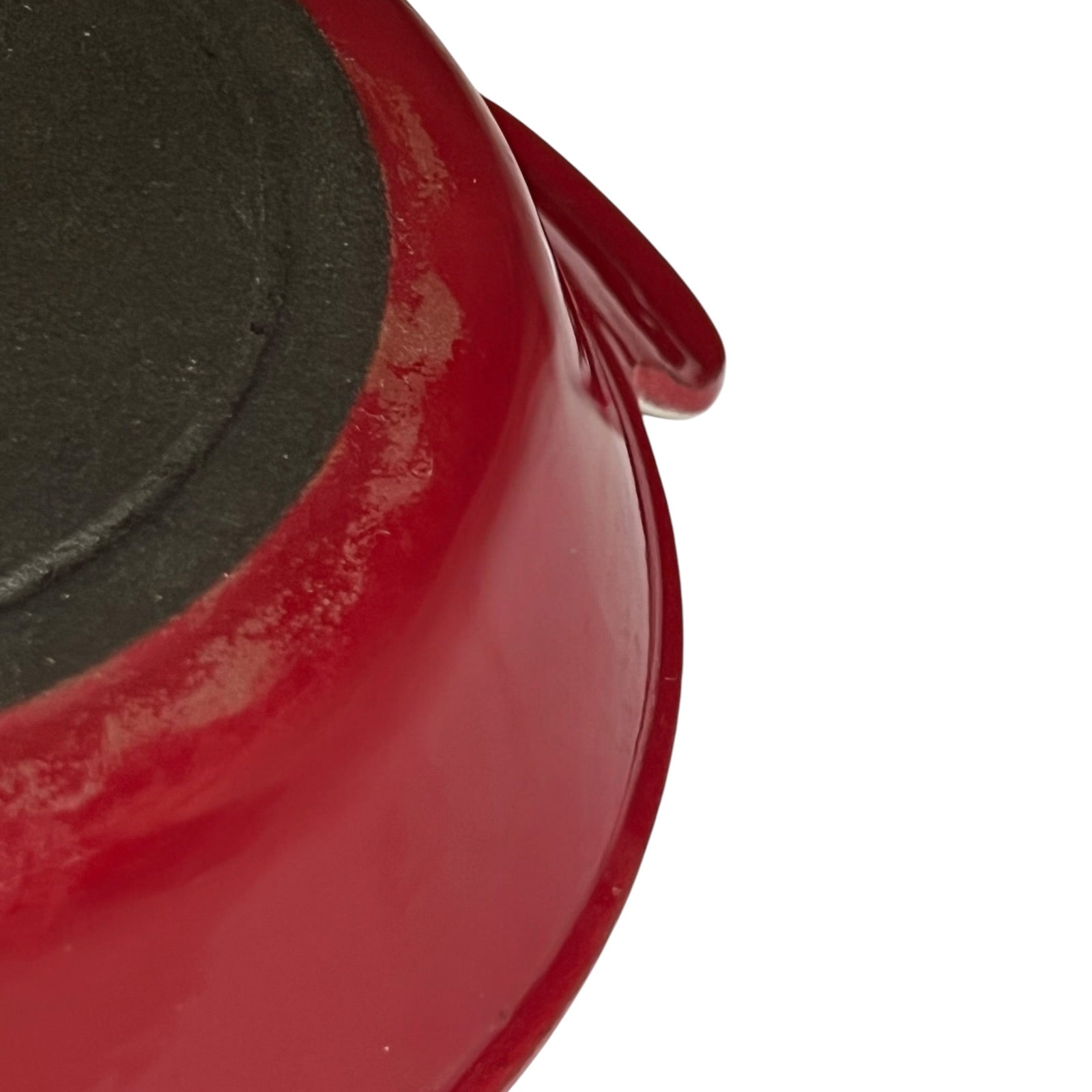 Close-up detail of a red enameled cast iron pot or pan showing the glossy red exterior and a dark non-stick coated interior, on a white background.