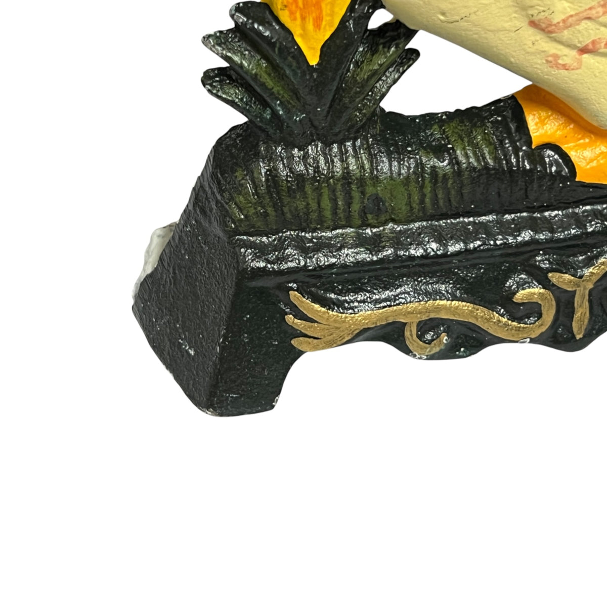 Close-up of a decorative object with a black textured base, gold scrollwork, green leaf-like detailing, and yellow-orange flame or leaf accents on a white background.