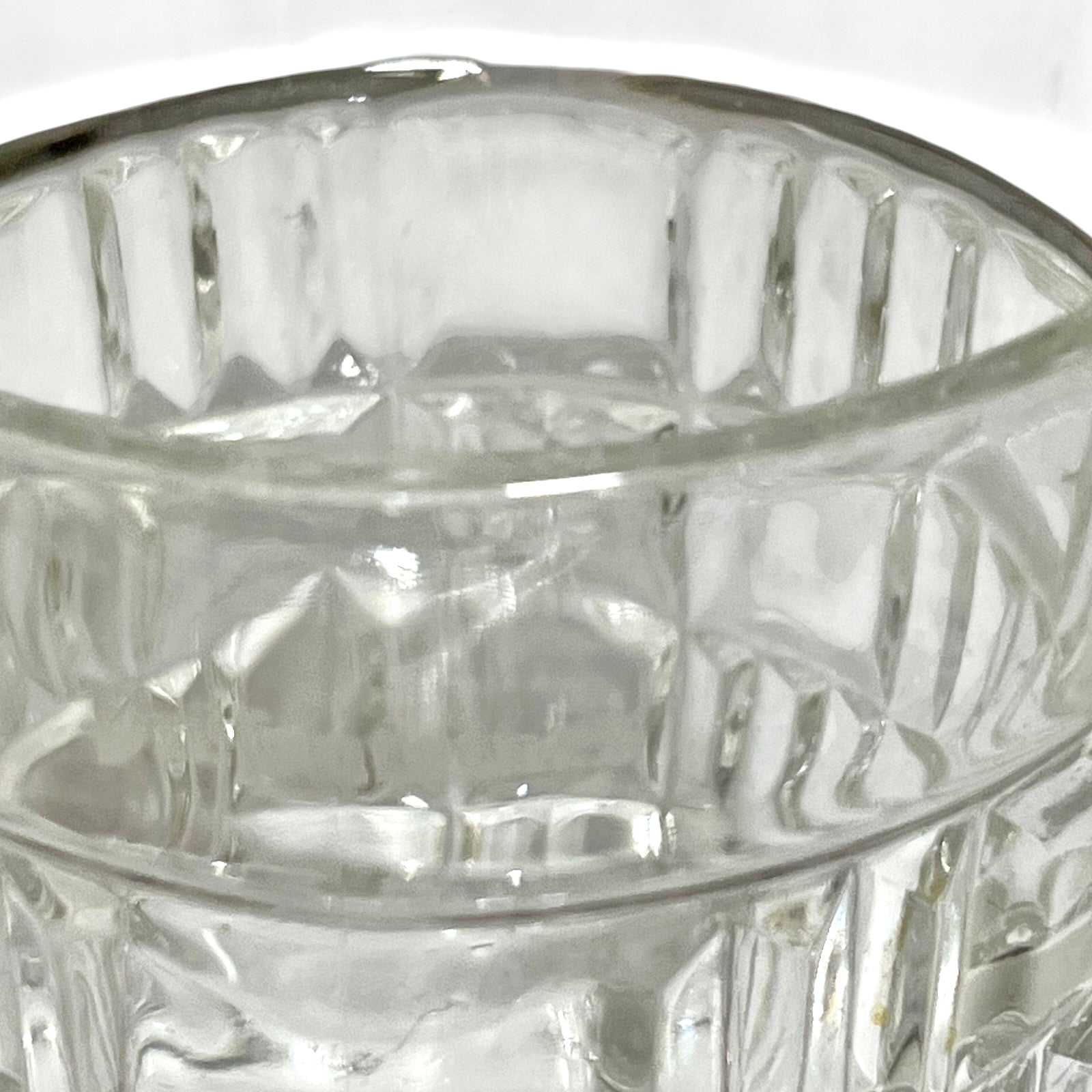 Close-up of a clear glass tumbler with a textured, vertically ribbed pattern and a polished silver-toned rim.