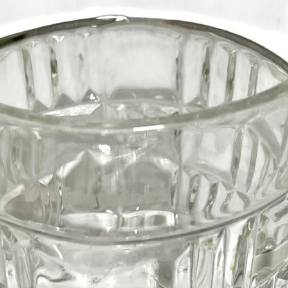 Close-up of a clear glass tumbler with a textured, vertically ribbed pattern and a polished silver-toned rim.