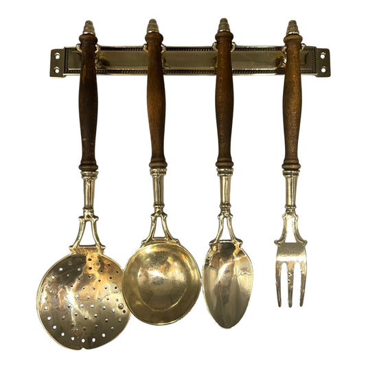 Set of four brass utensils with wooden handles on a brass rack against a white background