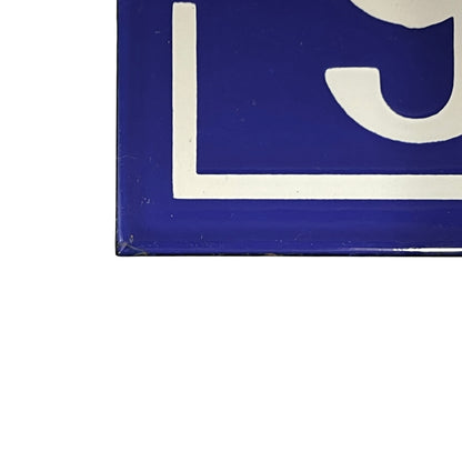 A close-up of a blue square sign or tile with a white painted border and partial white lettering, shown against a white background.