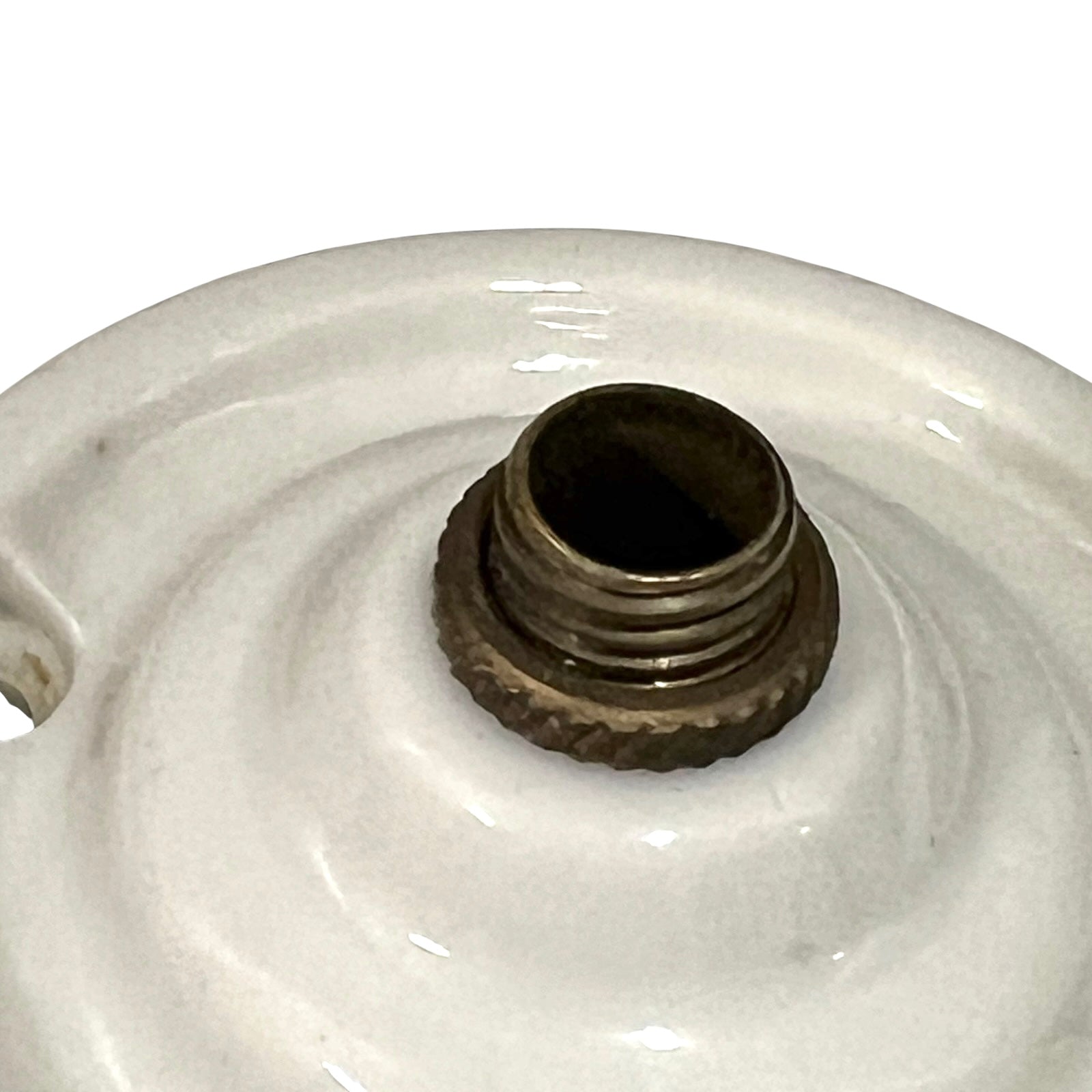 Close-up of a white ceramic lamp base or decorative ceramic object with a threaded metal fitting in the center, photographed against a plain white background.