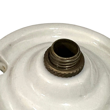Close-up of a white ceramic lamp base or decorative ceramic object with a threaded metal fitting in the center, photographed against a plain white background.