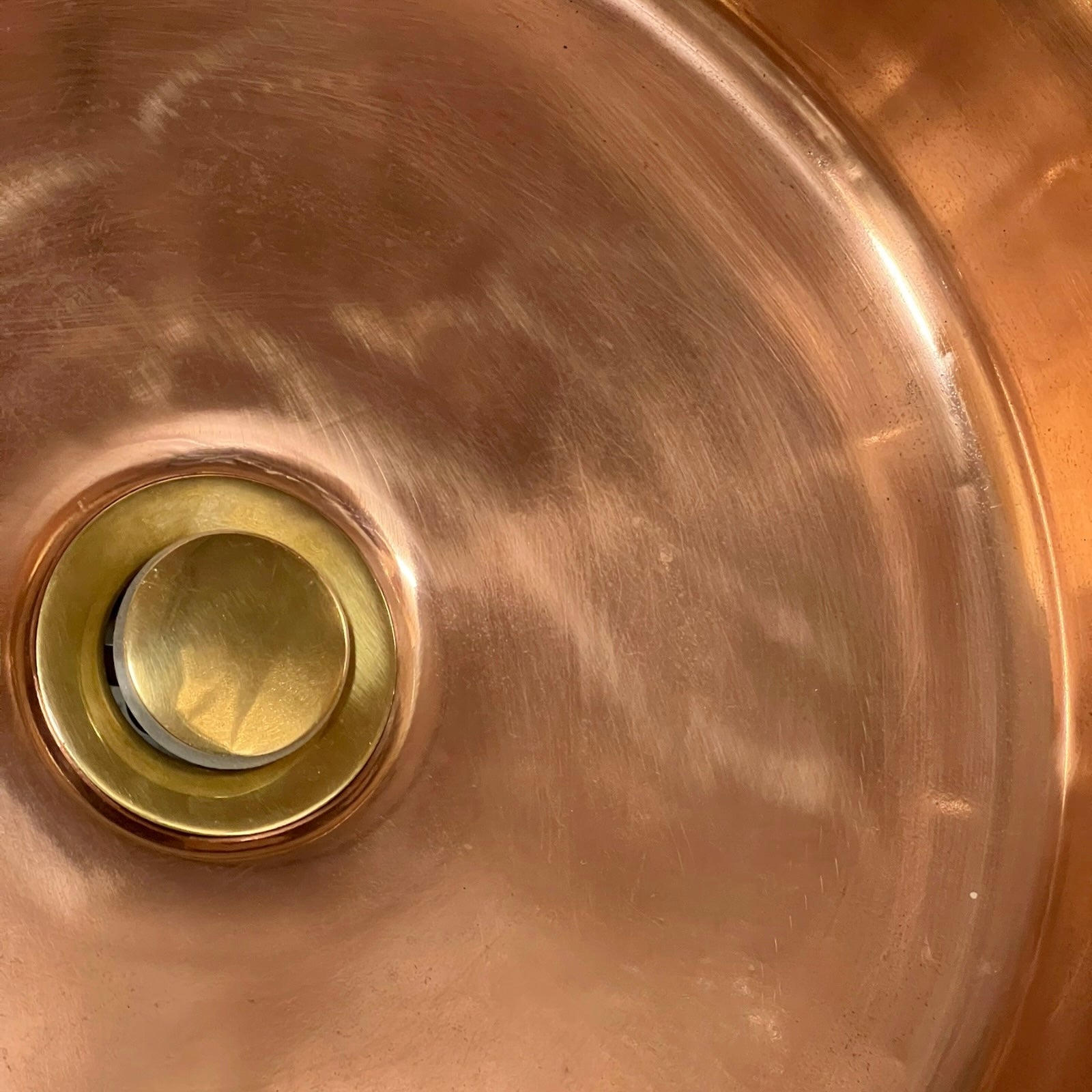 Close-up of a copper sink with a drain plug on a white background