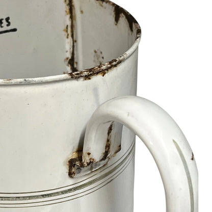 A close-up of a vintage white enamel pitcher with a curved handle, showing weathered rusted detailing along the rim and handle joint, on a white background.