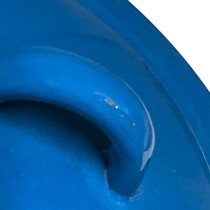 A close-up of a glossy bright blue curved object, showing a small white speck and a portion of a white background at the top right.