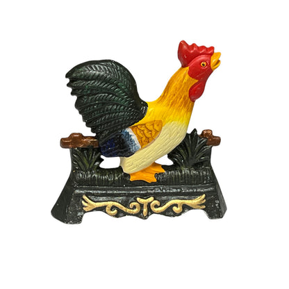 A decorative rooster doorstop figurine perched on a black ornate base, with a red comb and wattle, yellow and cream body, and dark green tail feathers, isolated on a white background.