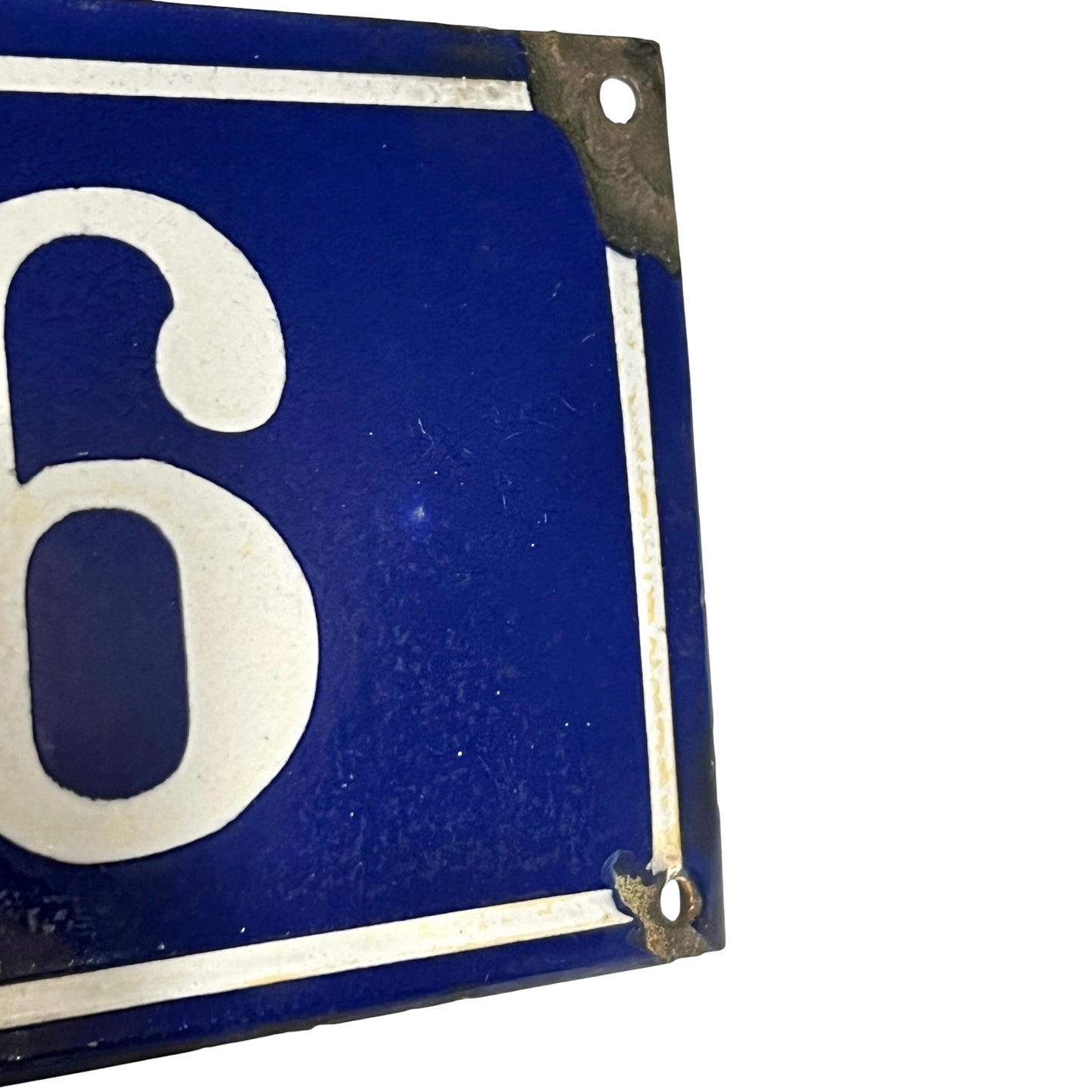 A close-up of a vintage-style blue enamel sign with a large white number 6 and white border lines, showing some wear and rust at the corners against a white background.