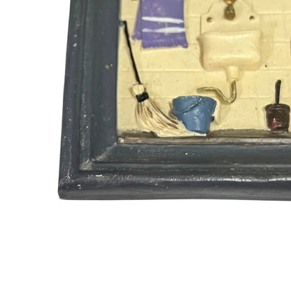 Small model of a bathroom scene with a toilet, sink, and other fixtures inside a framed display.