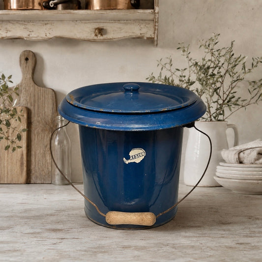 French vintage blue enamel bucket with a lid and a wooden handle on a wooden surface in a rustic kitchen setting. Ideal for a farmhouse or country kitchen setting