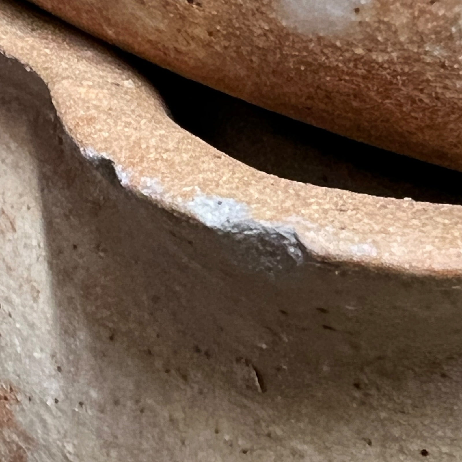 Close-up detail of a handmade terracotta clay vessel showing the textured, earthy brown surface and a white painted rim accent.