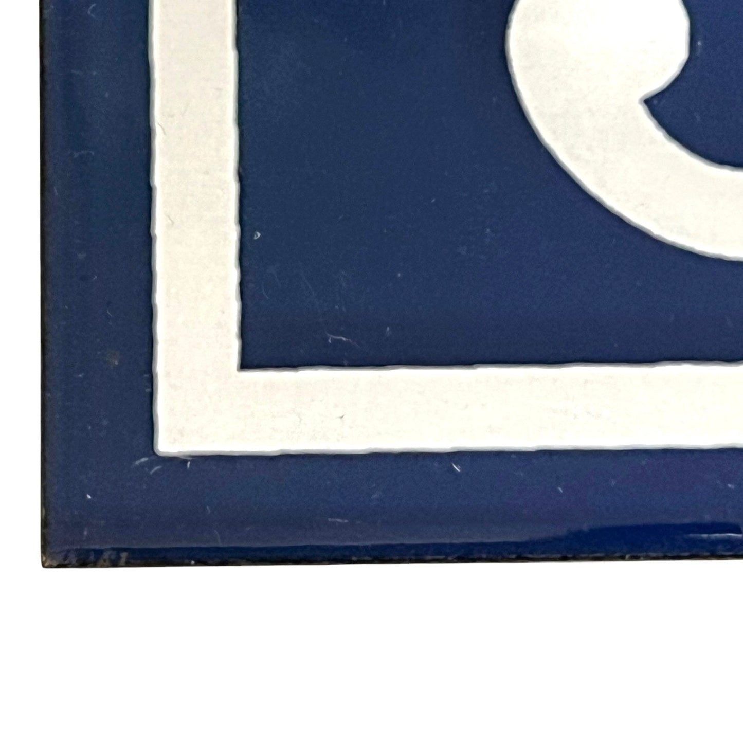 Close-up of a dark blue decorative tile or sign with a white border and partial white graphic, shown against a white background.