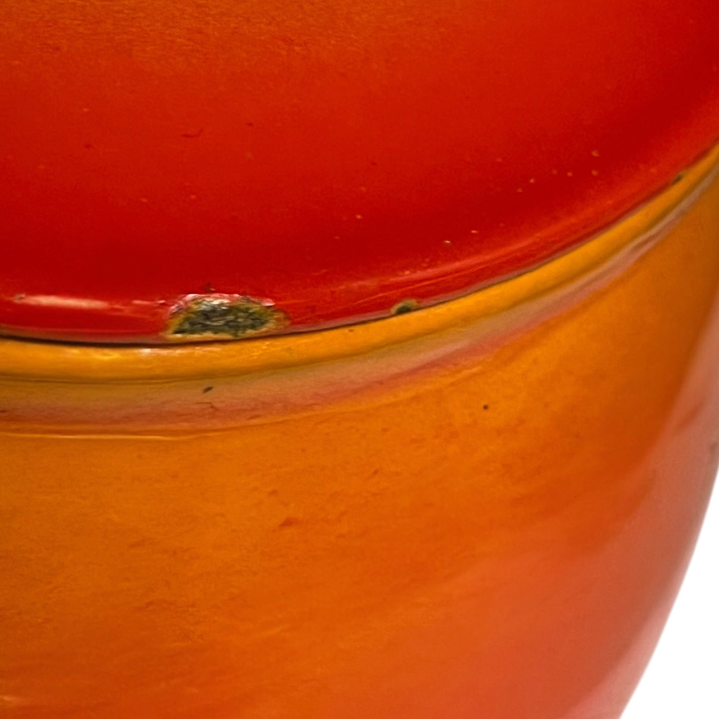 Close-up of a glossy ceramic pot or vase with a two-tone design, featuring a vibrant red upper section and a warm orange lower section.
