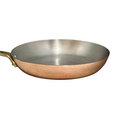 A copper saute pan with a brushed silver interior and a brass handle, shown from a side angle on a plain white background.