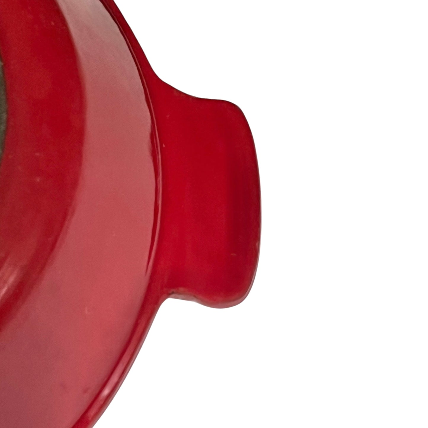 Close-up of a glossy red ceramic pot or casserole dish handle against a plain white background.
