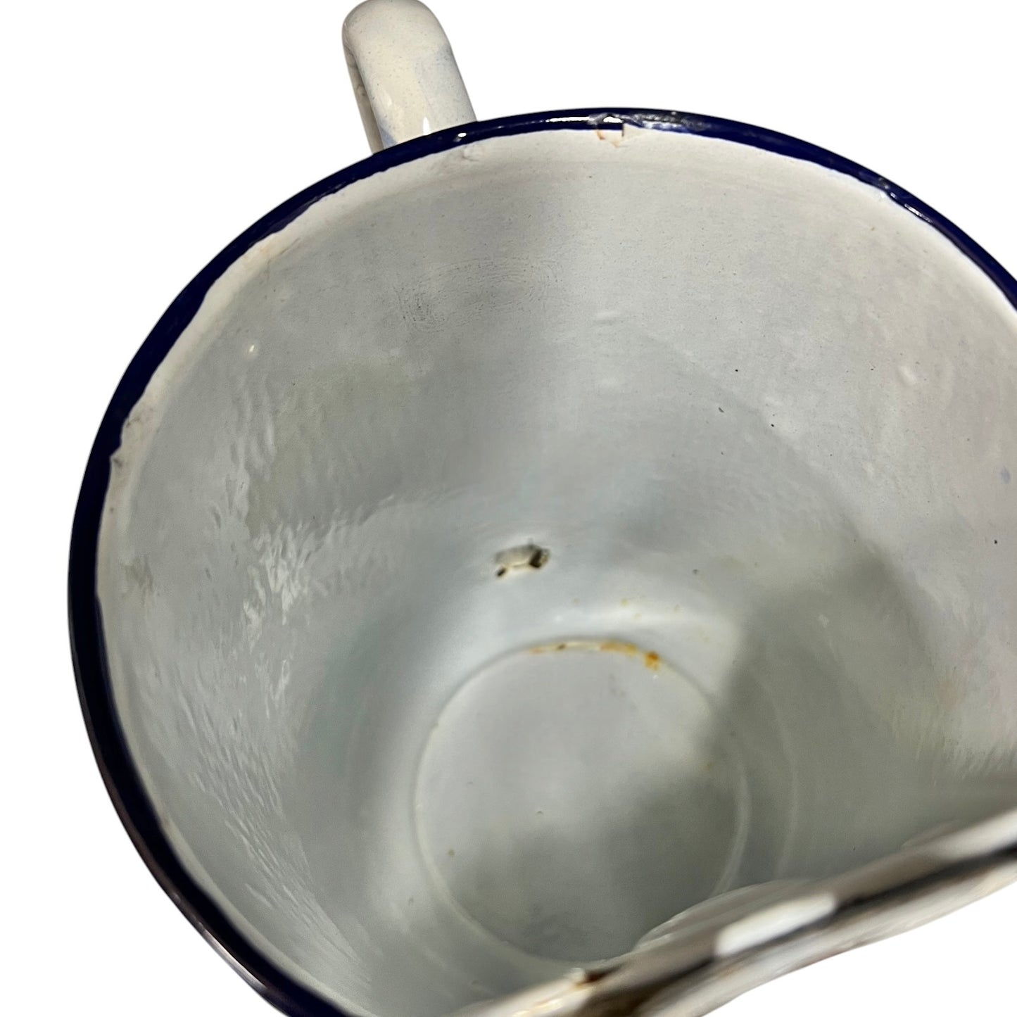 Close-up of the inside of a white enamel pot with a dark blue rim, showing a small hole near the top and a worn, vintage appearance.