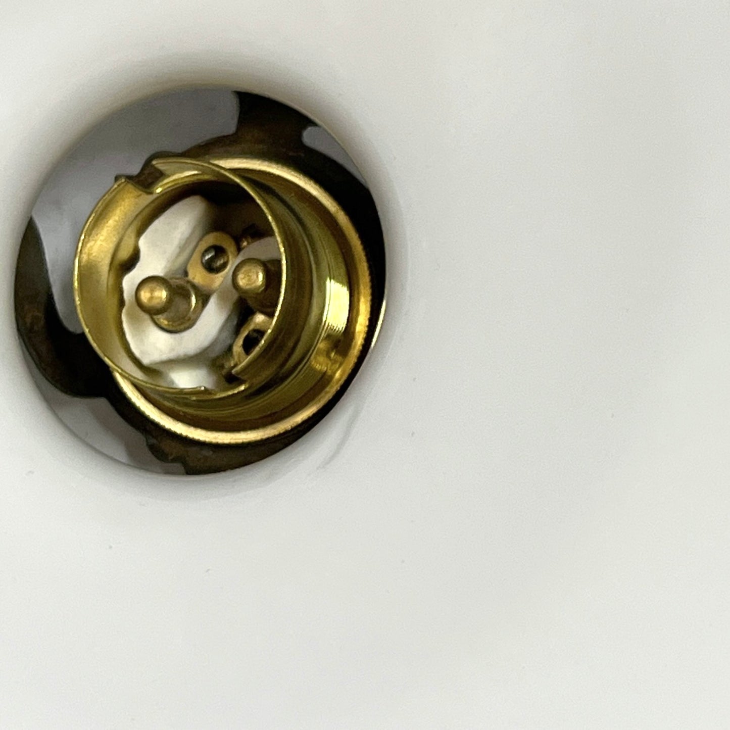 A close-up of a brass light bulb socket or electrical connector recessed into a white surface.