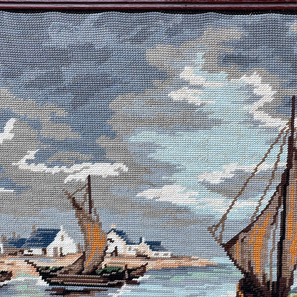 Close up of framed tapestry needlepoint with a coastal scene and wooden frame on a white background