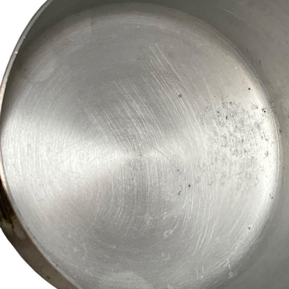 Close-up of the brushed metal interior of a round aluminum pot or pan, showing a silver finish with visible scratches and minor specks on the right side.