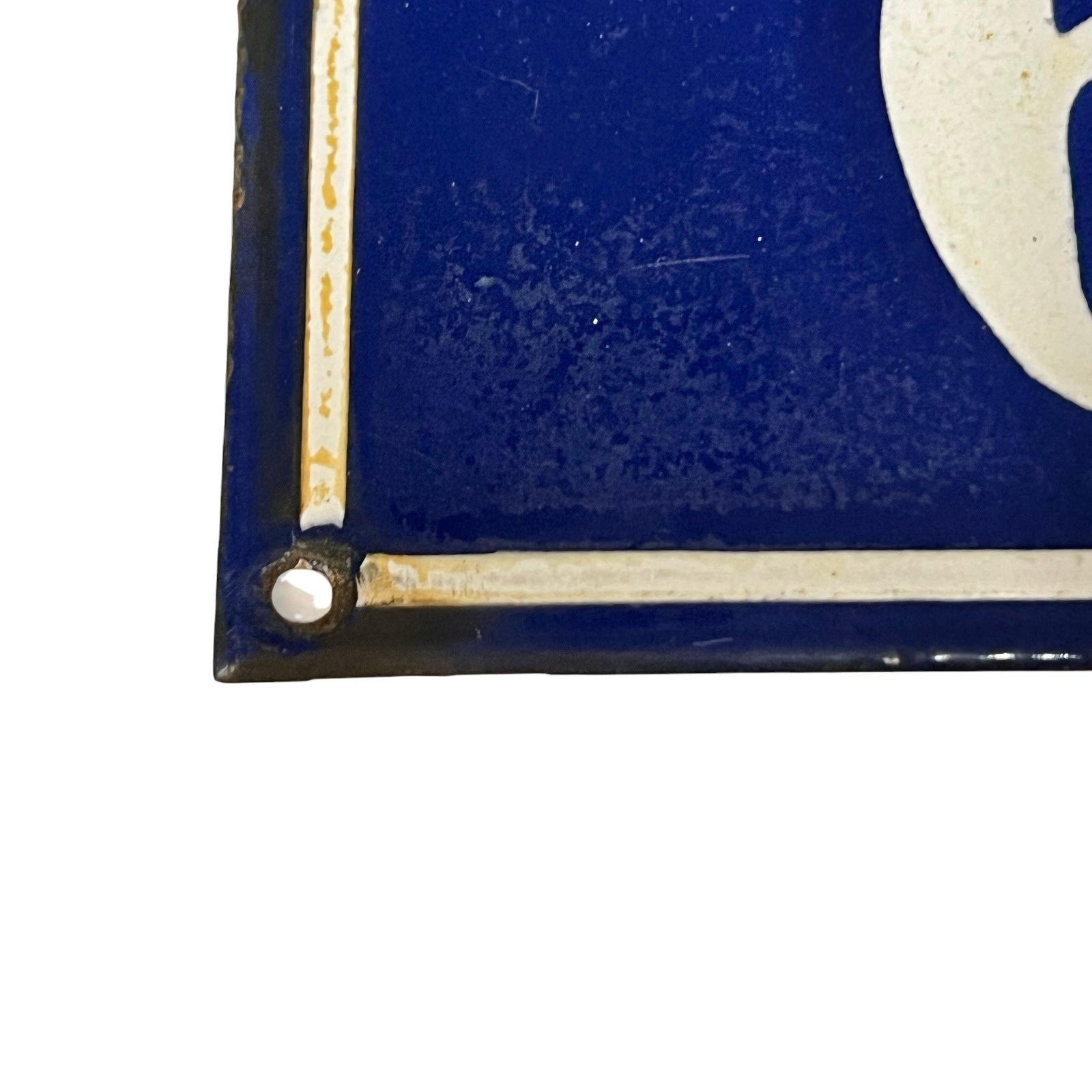 Close-up of a vintage blue enamel sign with a cream-colored border and a white mounting screw at the corner.