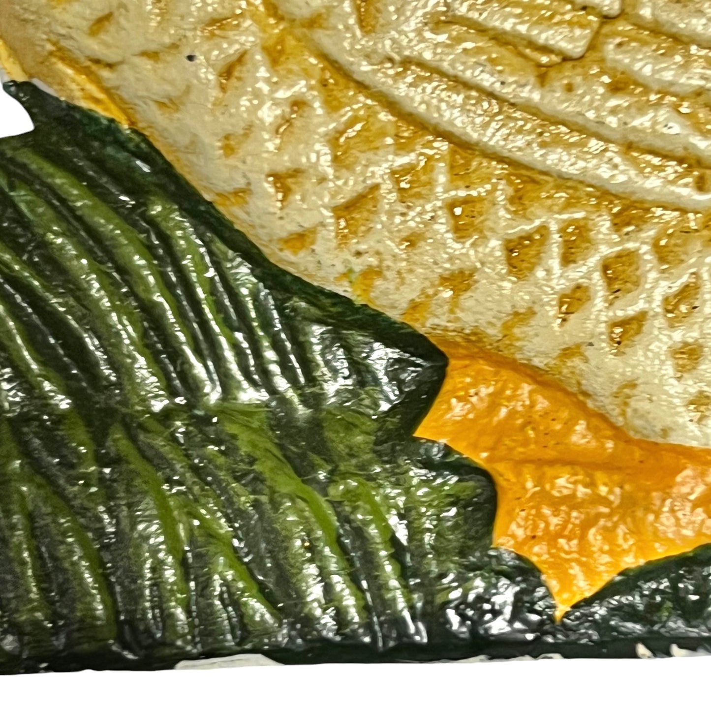 A close-up of a textured decorative surface featuring a dark green leaf-like form with glossy highlights, a warm orange section, and a cream-colored embossed patterned area.