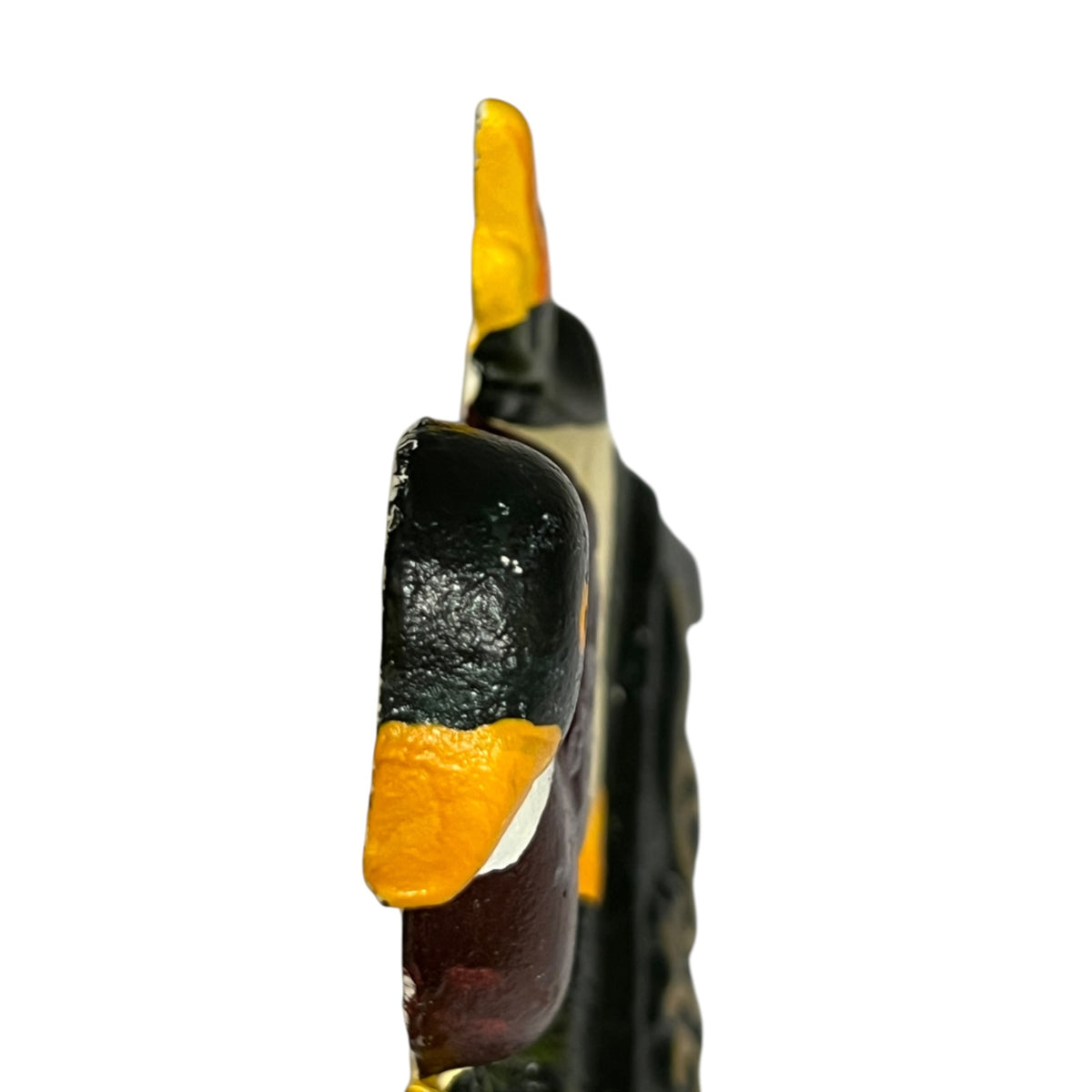 A close-up side view of a small door stop with a black body, bright yellow-orange sections, and a dark reddish-brown lower section, photographed against a plain white background.