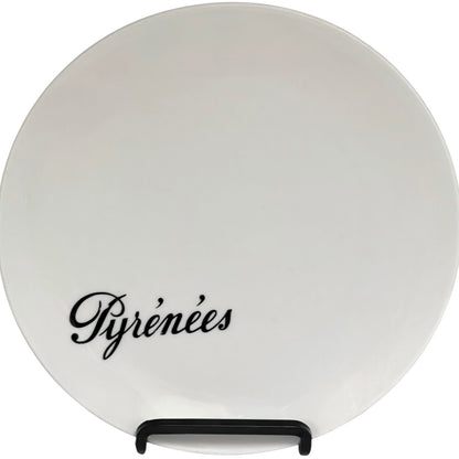 Round white plate with 'Pyrénèes' text on a stand against a white background