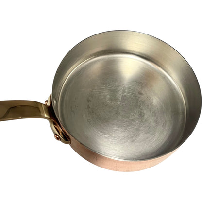 Small copper frying pan with a brass handle and tin lining on a white background