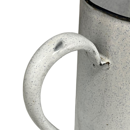 Close-up of an enamel jug with a speckled texture and handle on a white background