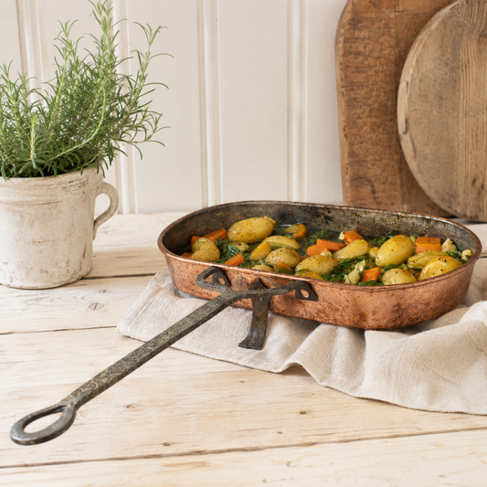 French antique copper hearth pan on a light wooden table filled with vegetables 